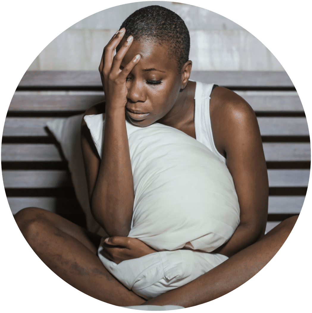 Woman sick with breast implant illness sitting in bed holding her head with her hand and clutching a pillow.
